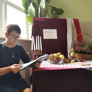 Zdjęcie  przedstawia nauczyciela-bibliotekarza czytającego fragment Moralności pani Dulskiej Gabrieli Zapolskiej na tle ekspozycji tematycznej z okazji Narodowego Czytania 2021