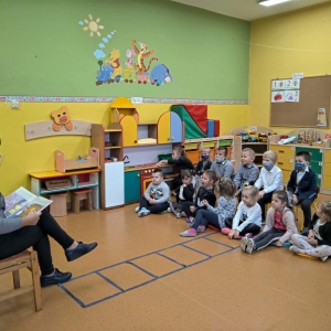 Zdjęcie przedstawia nauczyciela-bibliotekarza czytającego bajki dzieciom z przedszkola i z oddziału przedszkolnego w ramach obchodów Międzynarodowego Miesiąca Bibliotek Szkolnych.
